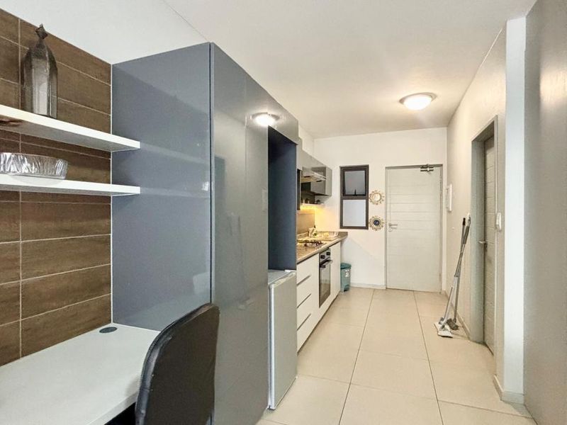 Modern kitchen featuring sleek grey cabinetry, integrated appliances, and a built-in workspace, complemented by neutral tiled flooring throughout.