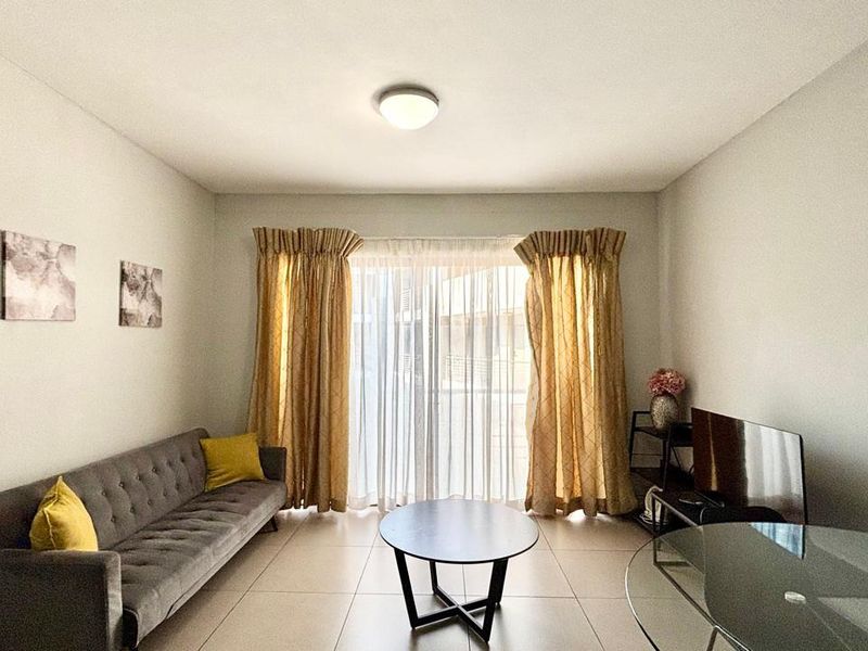 A well-lit living room featuring neutral tiled flooring and a large sliding glass door that provides access to the outdoor area.