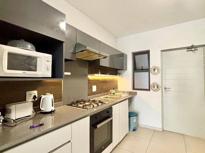 Modern kitchen featuring sleek grey and white cabinetry, stone countertops, gas hob, built-in oven, and integrated extractor fan with under-cabinet lighting.