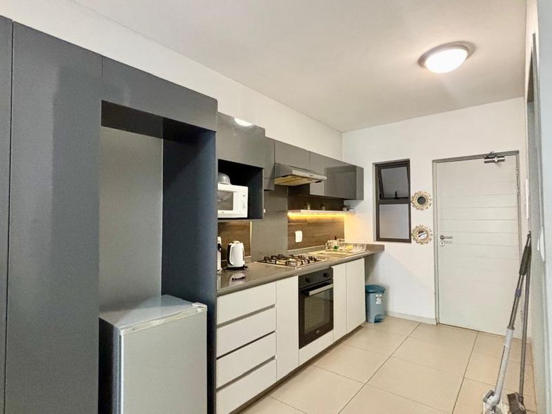 Modern kitchen featuring sleek grey and white cabinetry, stone countertops, integrated gas hob, oven, and extractor fan with contemporary under-cabinet lighting.