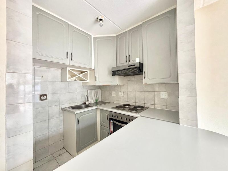 Compact kitchen featuring built-in cabinetry, tiled backsplash, electric hob, oven, and extractor fan, offering a functional layout ready for updates.