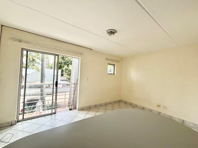 An empty bedroom featuring tiled flooring, a sliding glass door leading to a balcony, and neutral wall finishes.