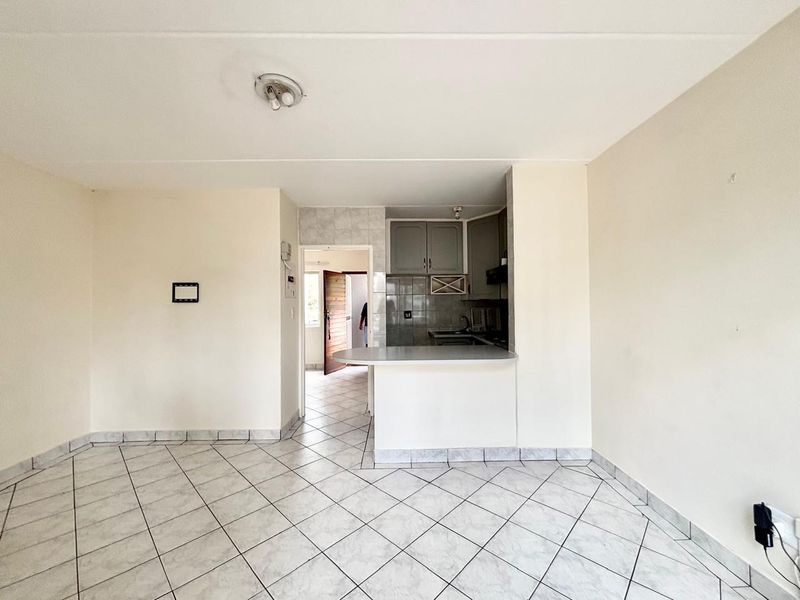 An open-plan living area featuring tiled flooring and a compact kitchen with built-in cabinetry and a breakfast bar.