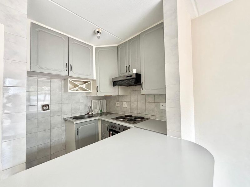 Compact kitchen featuring built-in cabinetry, electric hob, oven, extractor fan, and a breakfast counter, finished with tiled backsplash.