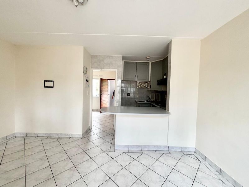 An open-plan living area featuring tiled flooring and a compact kitchen with built-in cabinetry, a breakfast bar, and tiled backsplash.
