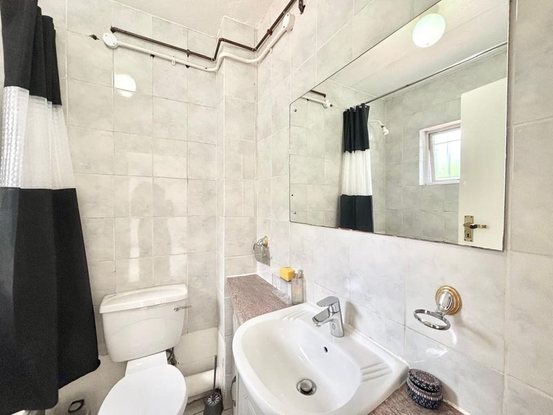 A compact bathroom featuring ceramic wall tiles, a vanity basin, and a toilet, with visible surface-mounted plumbing pipes.
