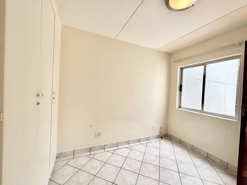 A vacant bedroom featuring tiled flooring, built-in cupboards, and a sliding window, providing a clean and neutral space ready for personalization.