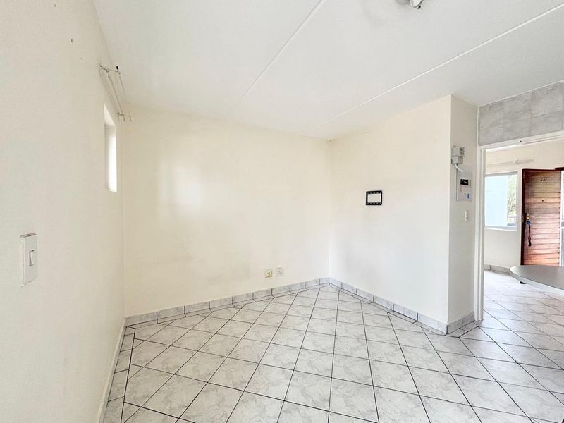 An empty, neutrally painted living area featuring tiled flooring and standard electrical fixtures, offering a blank canvas for interior design.