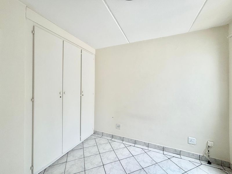 A clean, empty bedroom featuring neutral walls, tiled flooring, and built-in cupboards, providing a blank canvas for personalization.