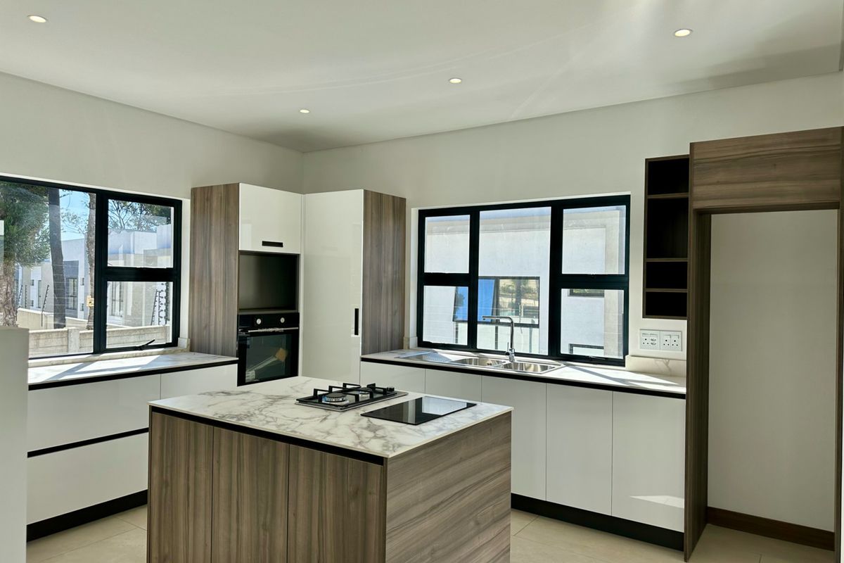 Modern kitchen featuring a central island with gas cooktop, built-in oven, stone countertops, and ample cabinetry, illuminated by recessed lighting and large windows.