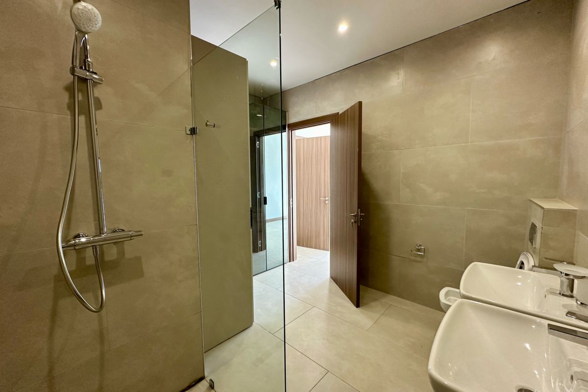Modern bathroom featuring a spacious walk-in shower with glass screen, dual vanity basins, and neutral floor-to-ceiling tiling.