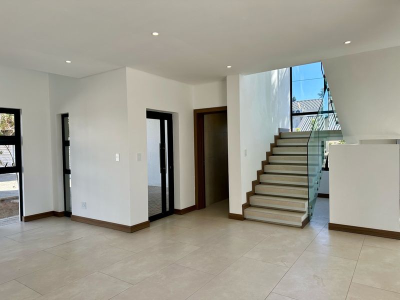 A bright and modern entrance hall featuring large format floor tiles, a contemporary staircase with glass balustrades, and clean architectural lines.
