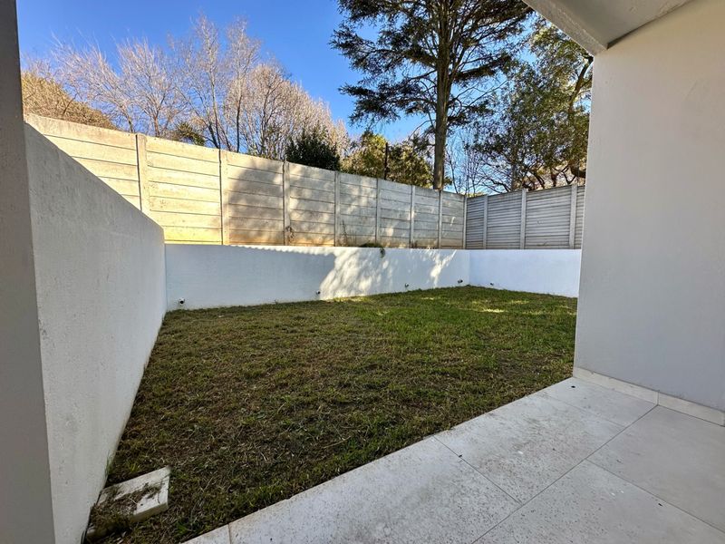 A private rear garden featuring a small lawn area, tiled patio, and secure precast concrete boundary walls.
