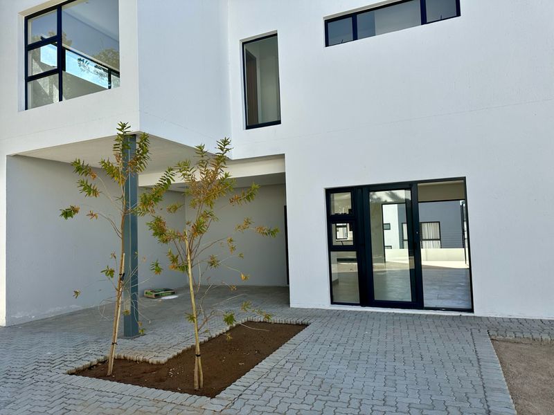 Modern townhouse rear elevation featuring clean white facade, paved courtyard area, and large aluminium-framed windows and sliding doors.