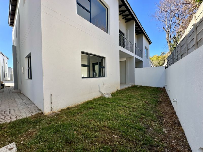 Rear view of the townhouse featuring a private garden area, paved walkway, and an upper-level balcony with modern aluminium window frames.