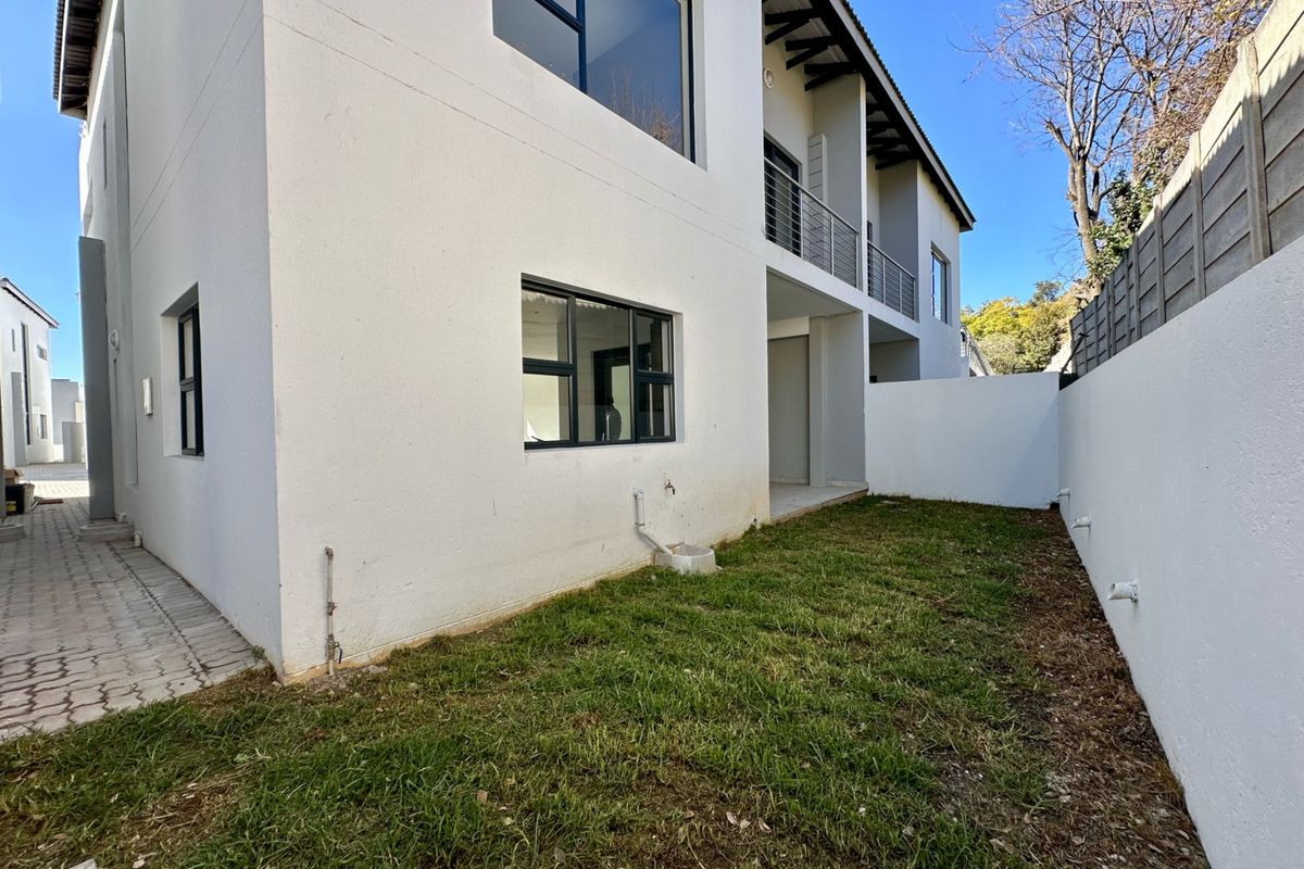 Rear view of the townhouse featuring a private garden area, paved walkway, and an upper-level balcony with modern aluminium window frames.