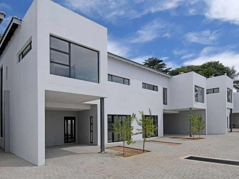 Modern townhouse complex featuring clean white facades, paved driveway, and covered parking areas with contemporary aluminum window frames.