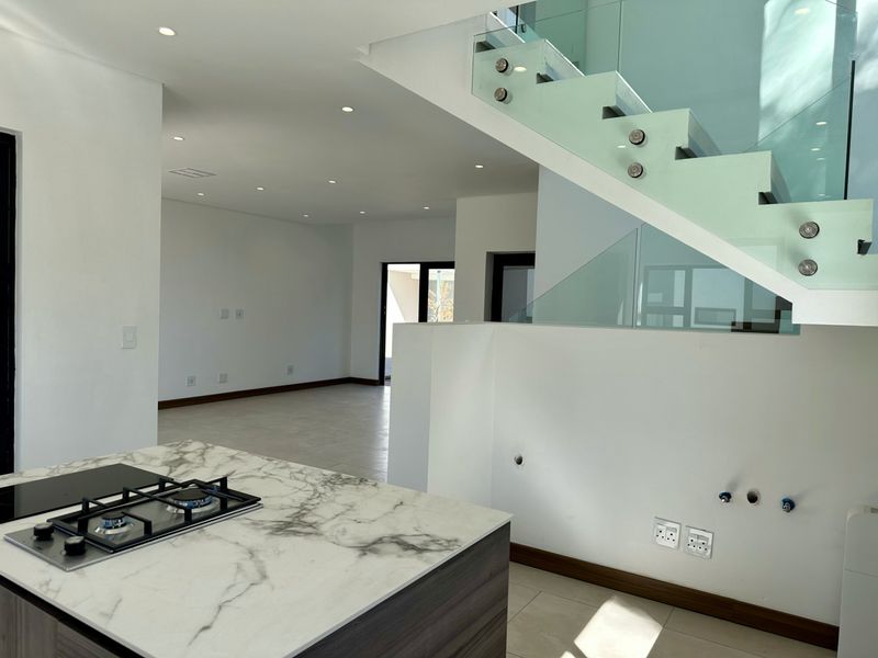 Modern open-plan living area featuring a marble-look kitchen island with gas hob and a contemporary staircase with glass balustrade.