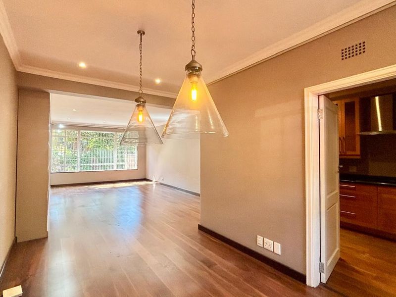 Spacious open-plan living area featuring polished hardwood floors, recessed and pendant lighting, and a view into the adjacent kitchen with built-in cabinetry.