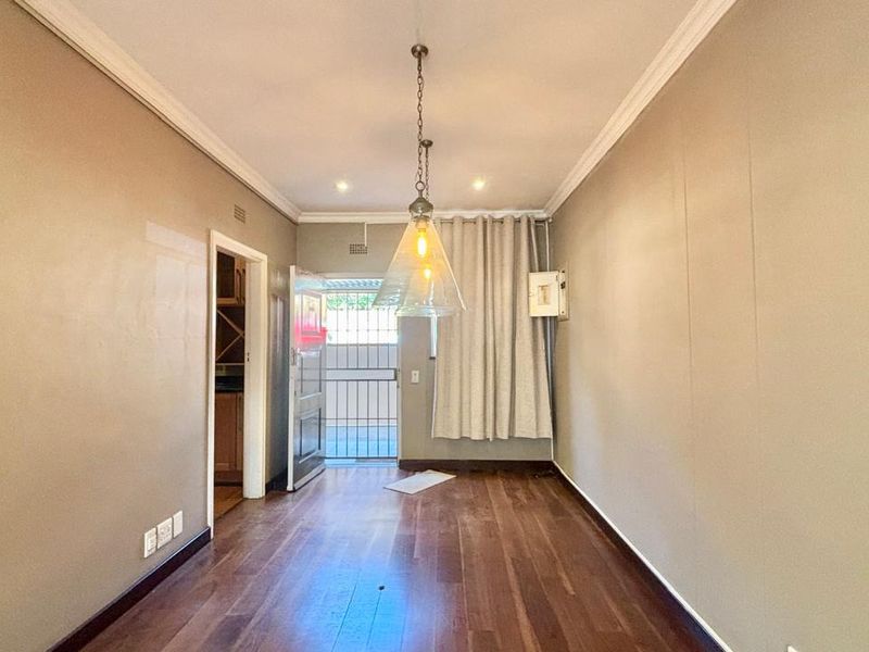 An empty living area featuring hardwood flooring, crown molding, and a pendant light fixture, with direct access to an exterior security gate.
