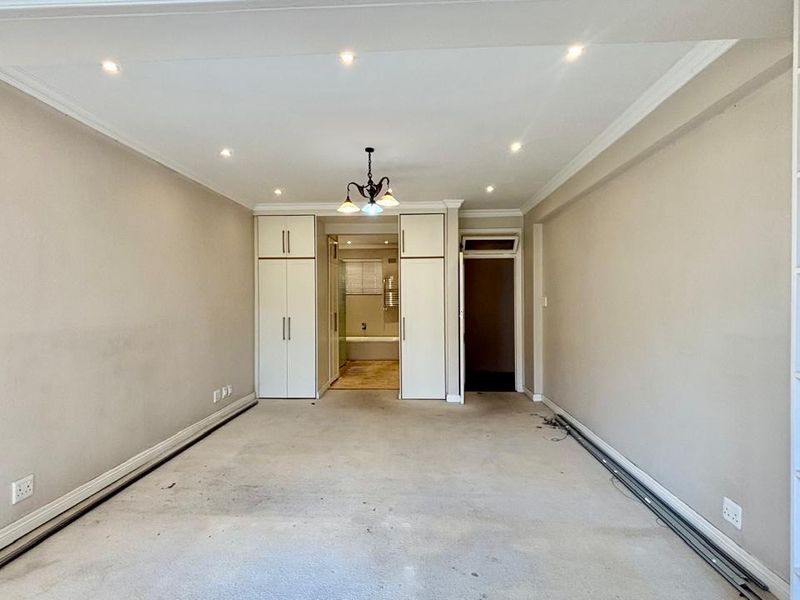 An empty bedroom featuring built-in cupboards, integrated shelving, and recessed lighting, requiring cosmetic updates to the flooring and wall finishes.