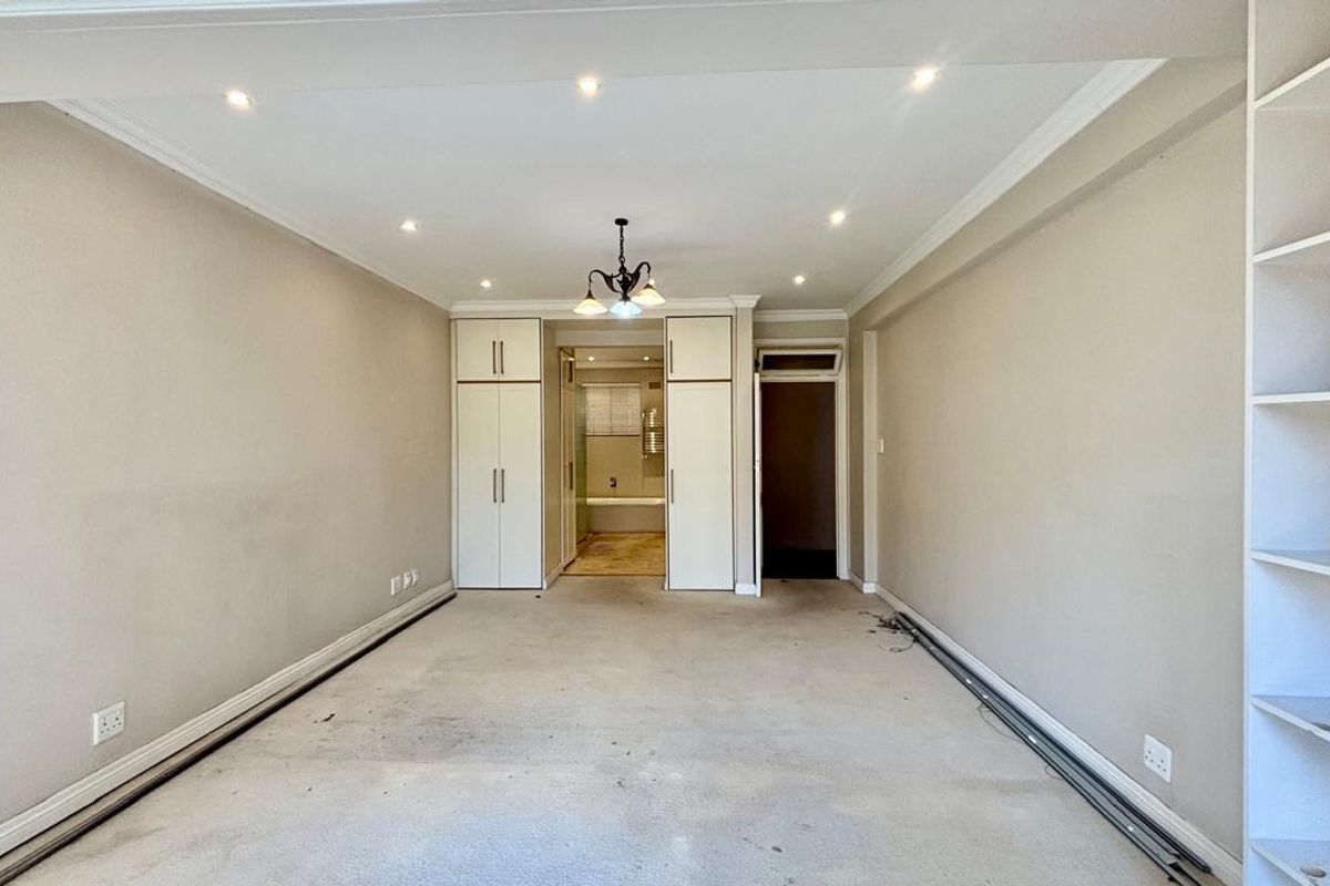 An empty bedroom featuring built-in cupboards, integrated shelving, and recessed lighting, requiring cosmetic updates to the flooring and wall finishes.