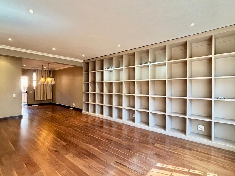 Spacious living area featuring polished hardwood flooring, extensive built-in shelving, and recessed lighting, offering a clean and versatile space.