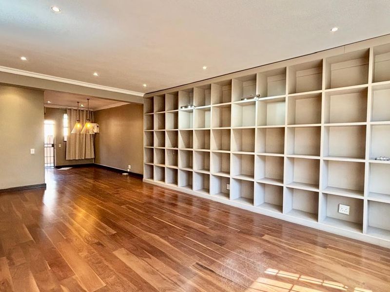 Spacious living area featuring polished hardwood flooring, recessed lighting, and an extensive floor-to-ceiling built-in shelving unit.