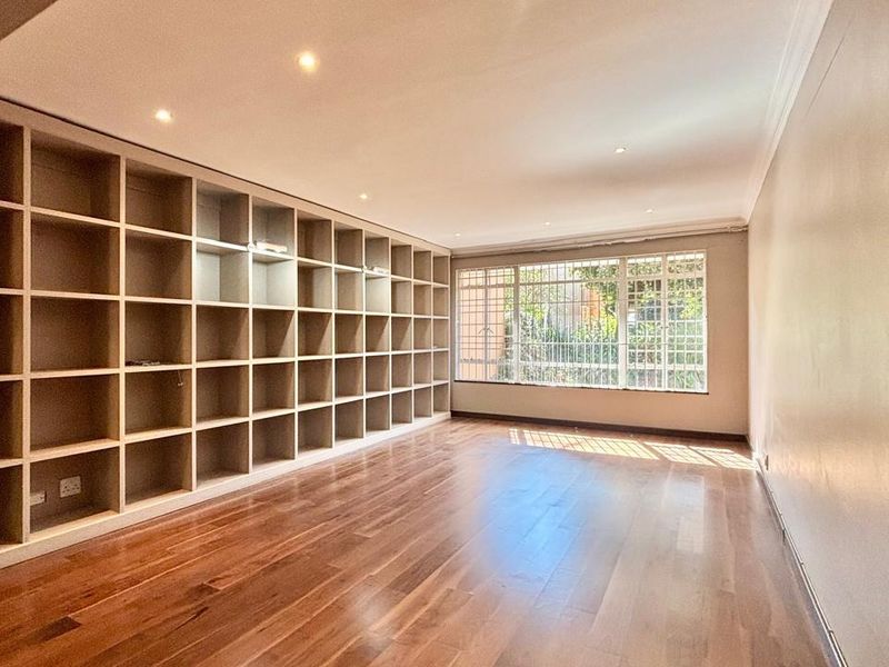 Spacious living area featuring extensive built-in shelving, warm hardwood flooring, and recessed lighting, offering a versatile space for a library or lounge.