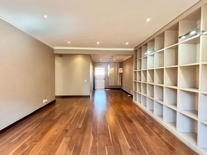 Spacious living area featuring polished hardwood flooring, recessed downlighting, and an extensive floor-to-ceiling built-in shelving unit.