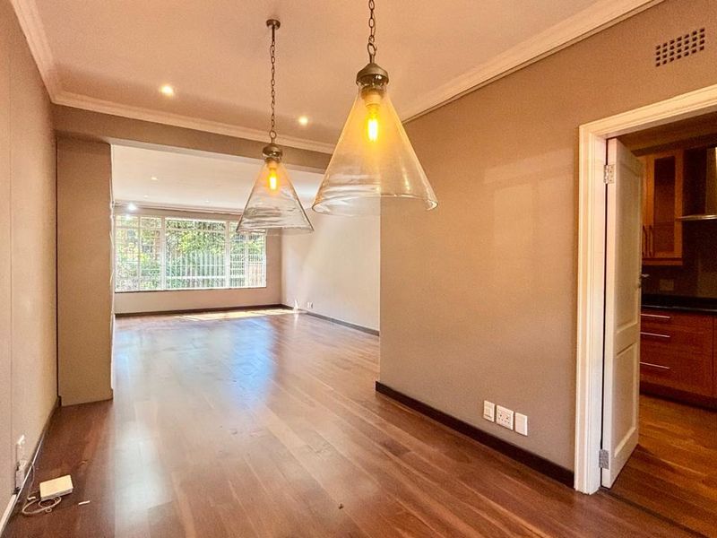 Spacious open-plan living area featuring polished hardwood floors, modern pendant lighting, and seamless flow into a well-appointed kitchen with built-in cabinetry.
