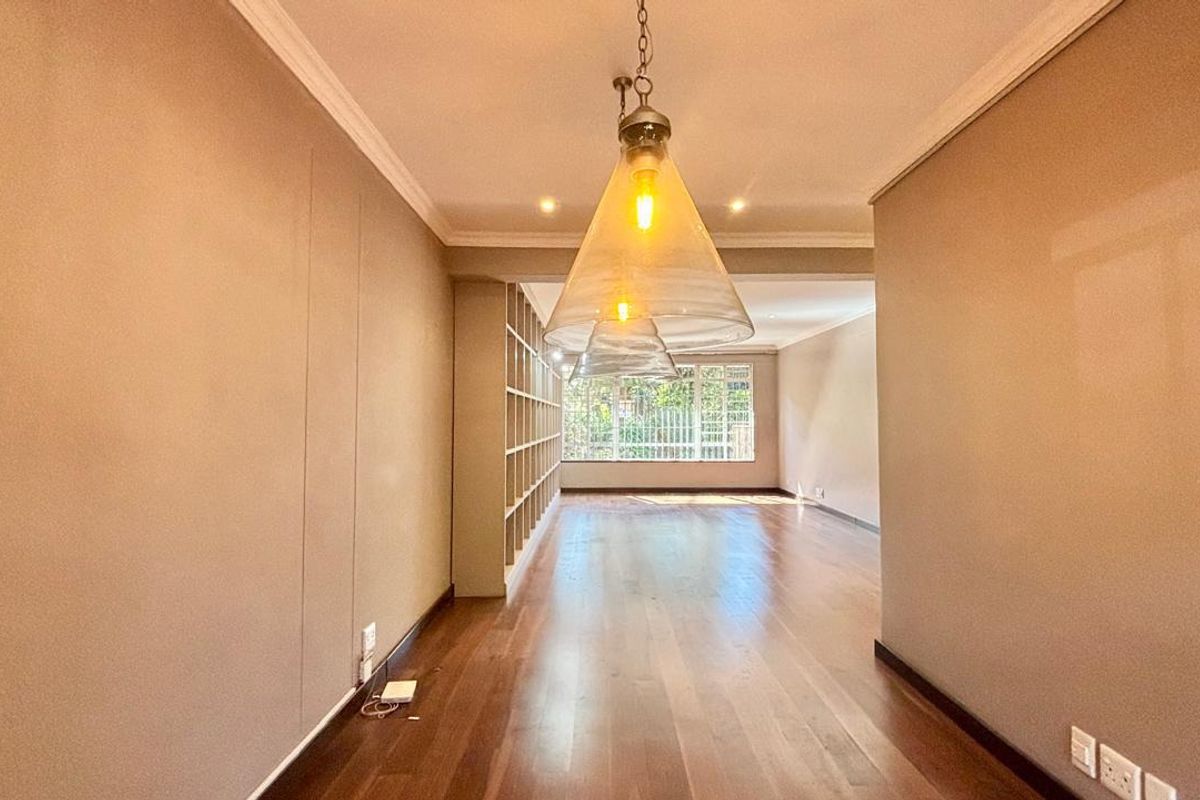 Spacious living area featuring polished hardwood flooring, built-in shelving, and elegant pendant lighting, offering a bright and versatile open-plan layout.