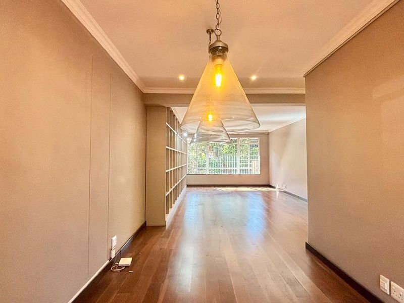 Spacious living area featuring polished hardwood flooring, built-in shelving, and elegant pendant lighting, offering a bright and versatile open-plan layout.