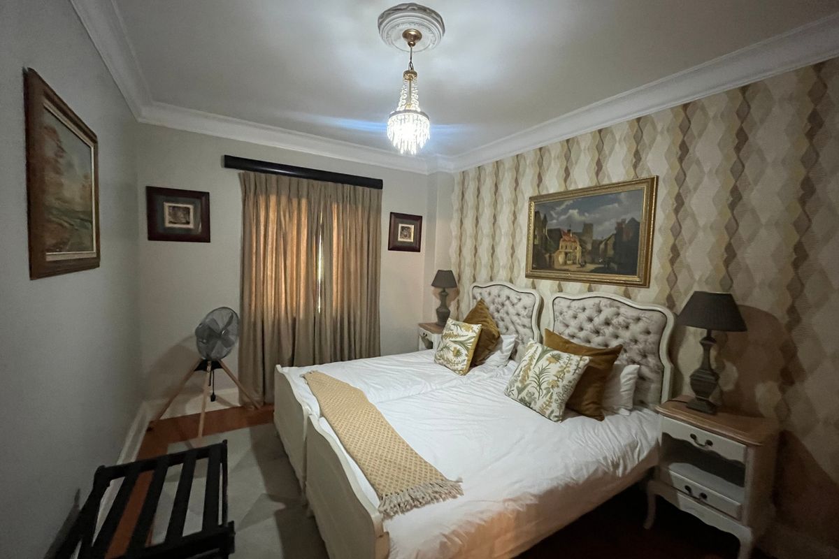 A well-maintained bedroom featuring decorative coving, a central ceiling rose with a chandelier, and warm hardwood flooring.