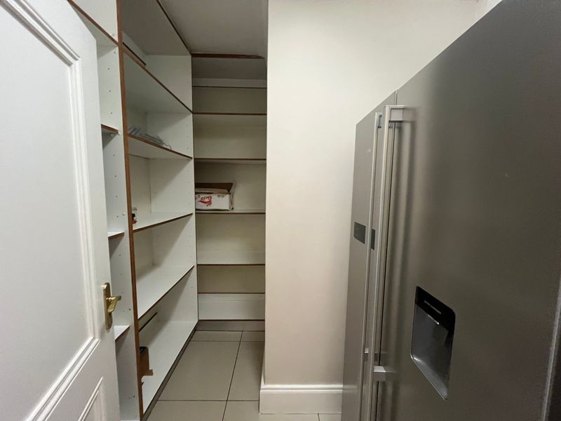 A functional scullery or pantry area featuring extensive built-in shelving and tiled flooring, providing ample storage space.