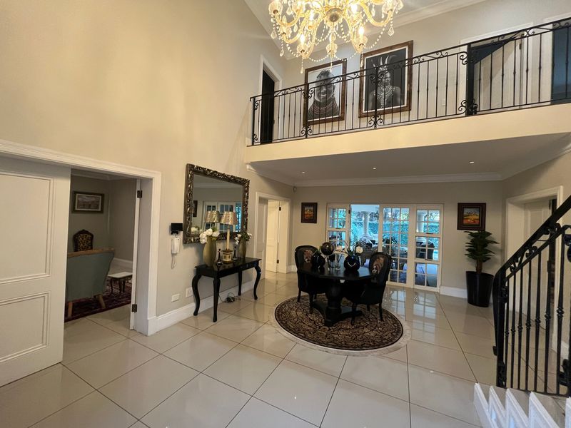 Spacious double-volume entrance hall featuring a grand staircase, wrought iron mezzanine balustrade, elegant crystal chandelier, and polished tiled flooring leading to the living areas.