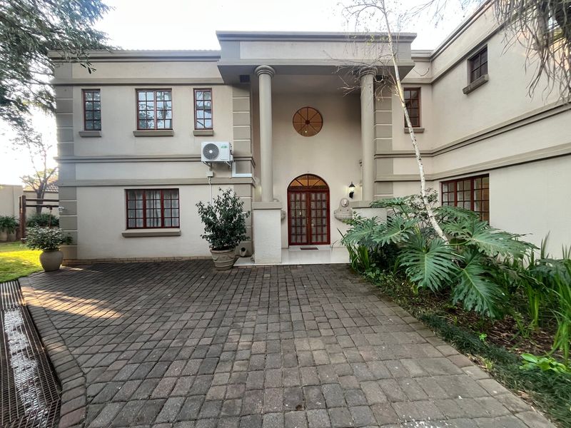 Front elevation of a double-storey residence featuring a paved driveway, portico entrance with columns, and timber-framed windows and doors.