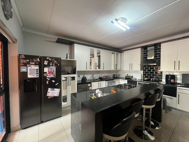 Modern kitchen featuring white cabinetry, black granite countertops, a central island with breakfast bar, gas hob, and stylish subway tile backsplash.