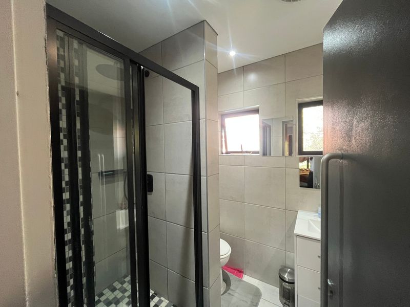 Modern bathroom featuring a walk-in shower with black-framed glass enclosure, neutral wall tiling, and a vanity unit with integrated basin.