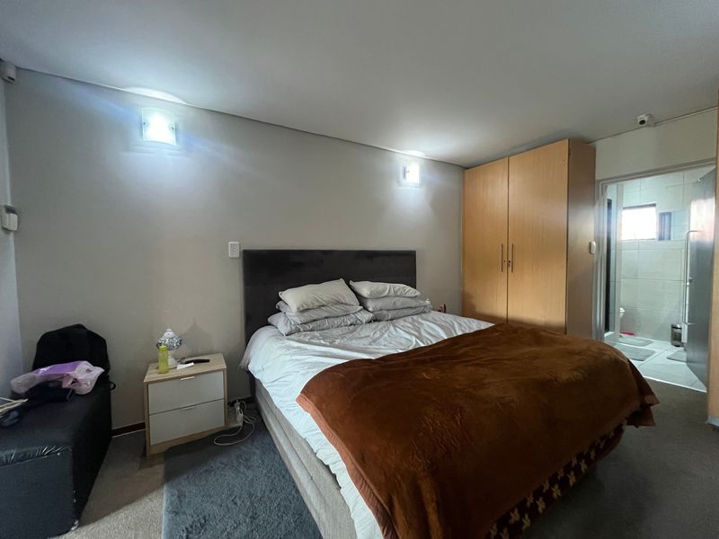 A bedroom featuring a built-in wooden wardrobe and wall-mounted lighting, with an adjoining en-suite bathroom visible through the doorway.
