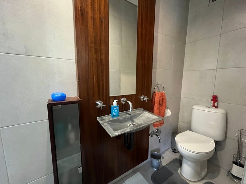 A modern bathroom featuring a wall-mounted basin with a wood-veneer panel, integrated mirror, and neutral wall tiling.
