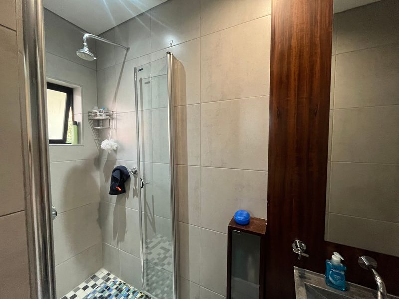 Modern bathroom featuring a glass-enclosed shower with mosaic floor tiling, neutral wall tiles, and a sleek vanity area with a mirror.