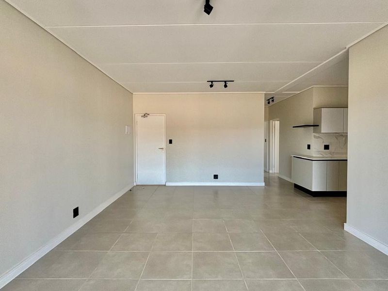 Spacious open-plan living area featuring neutral tiled flooring, modern track lighting, and a sleek, minimalist kitchen with built-in cabinetry.