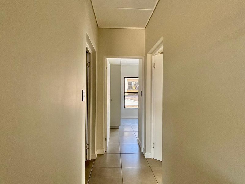 A clean, neutral hallway with tiled flooring, connecting multiple rooms within the apartment.