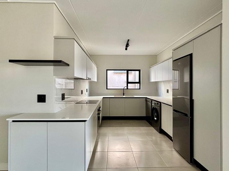 Modern, minimalist kitchen featuring sleek white cabinetry, stone countertops, integrated appliances, and neutral tiled flooring in a clean, well-lit space.