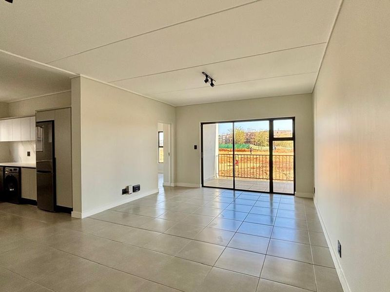 Modern open-plan living area featuring tiled floors, track lighting, and a seamless transition to a private balcony through large sliding glass doors.