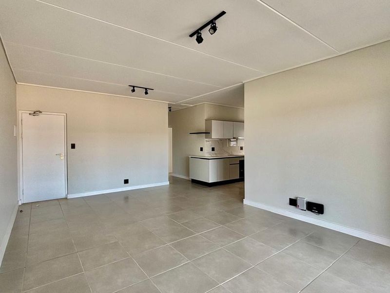 Spacious open-plan living area featuring neutral tiled flooring, modern track lighting, and a compact kitchen with built-in cabinetry and an extractor fan.