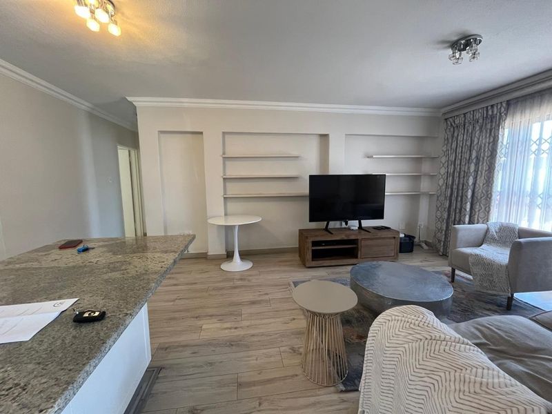 Open-plan living area featuring laminate flooring, built-in shelving, and a granite kitchen island, creating a functional and connected space.