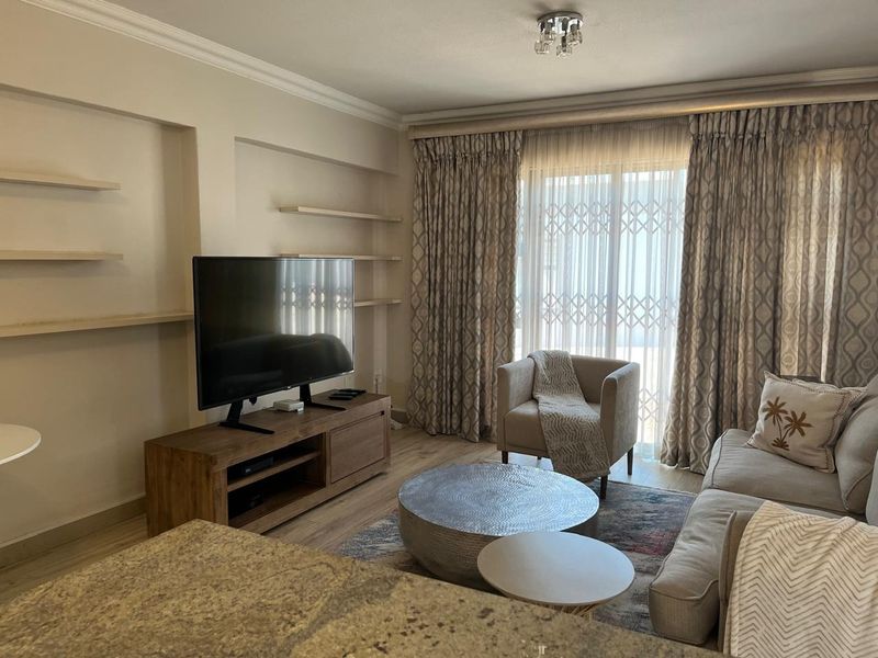 A comfortable living room featuring built-in wall shelving, recessed niches, laminate flooring, and a sliding glass door with security gate leading to the exterior.