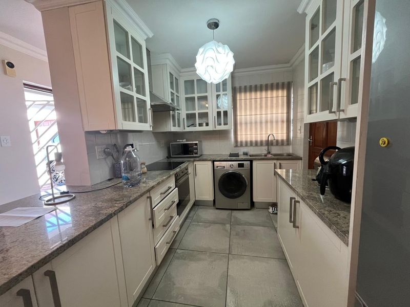 A functional kitchen featuring granite countertops, built-in cabinetry, integrated oven and hob, and tiled flooring, offering a clean and practical workspace.